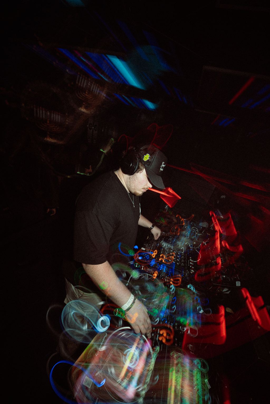 DJ mixing at the booth, hands on the controller under colorful motion-blurred lighting