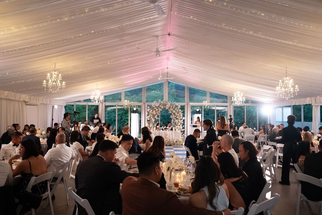 Reception tent set for dinner under string lights and chandeliers