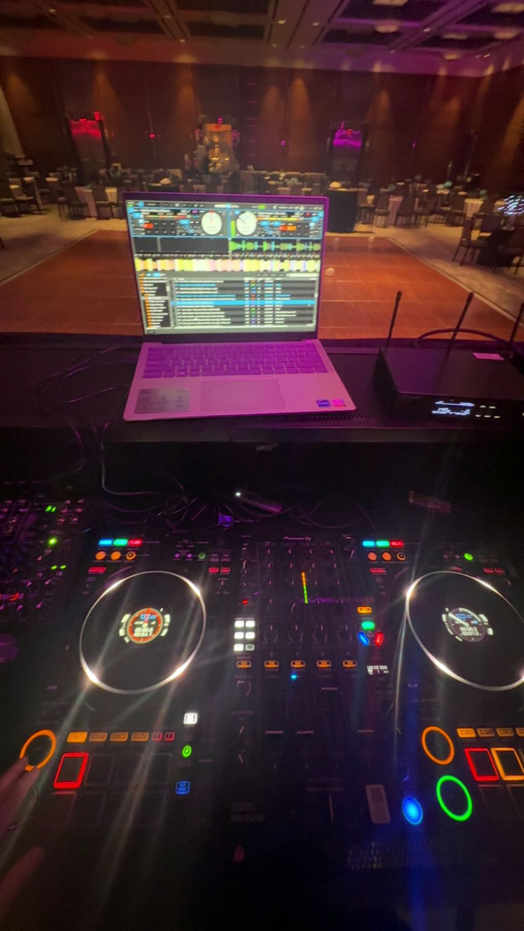 DJ laptop and mixer glowing under purple stage lighting
