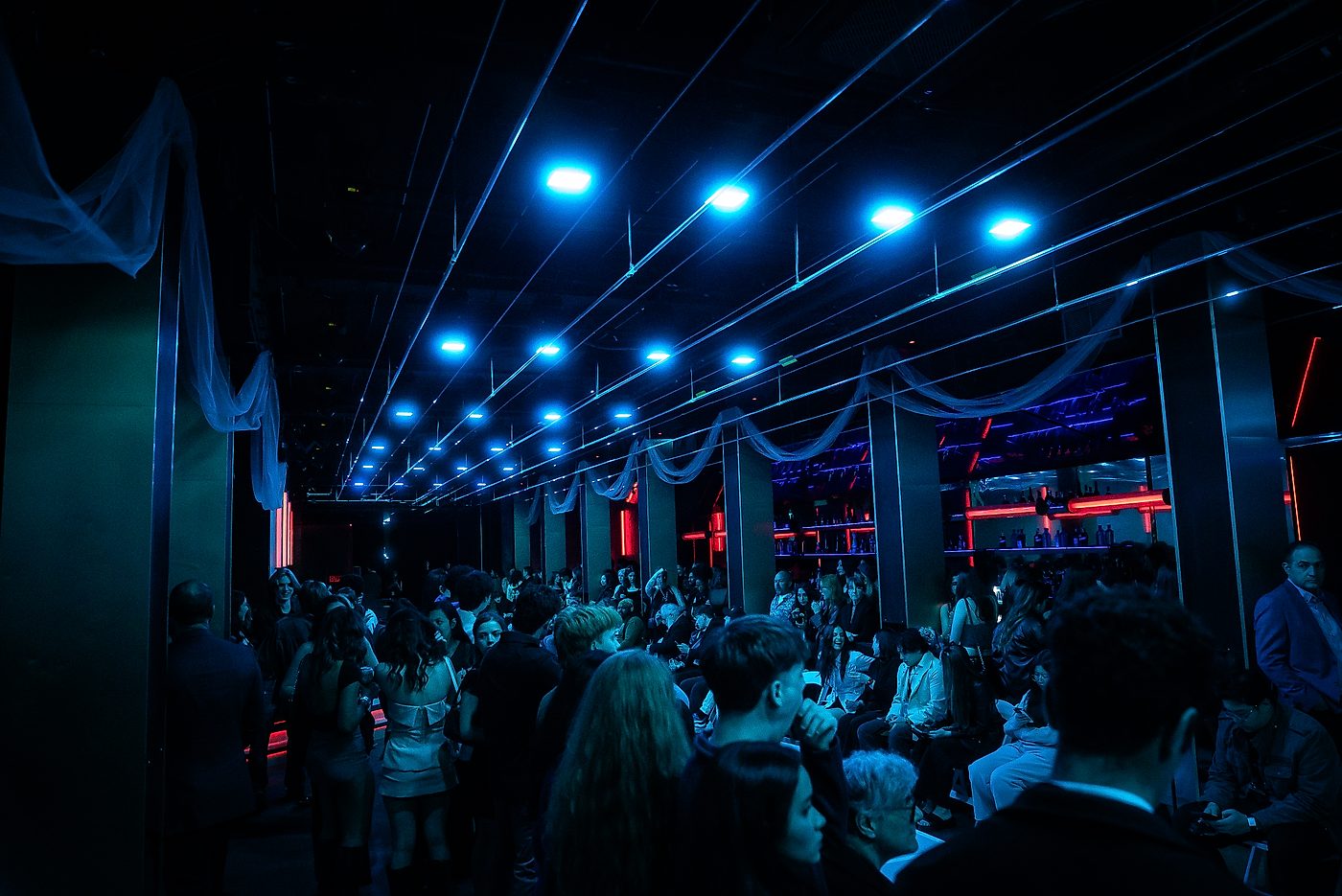 Guests seated along a lit corridor beneath dramatic blue overhead lighting